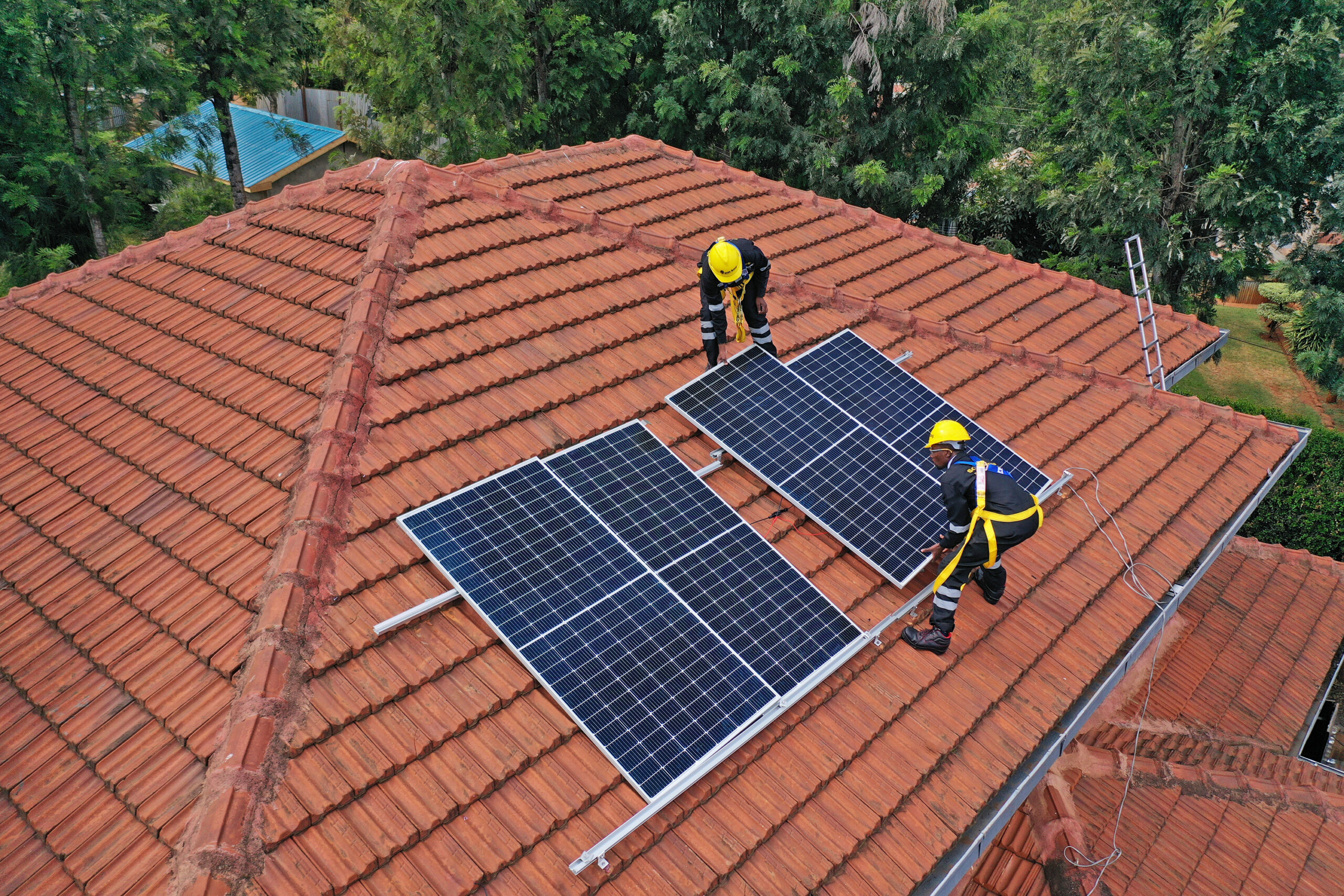 Image shows two Sun King employees wearing PPE installing solar panels on the roof of a house.