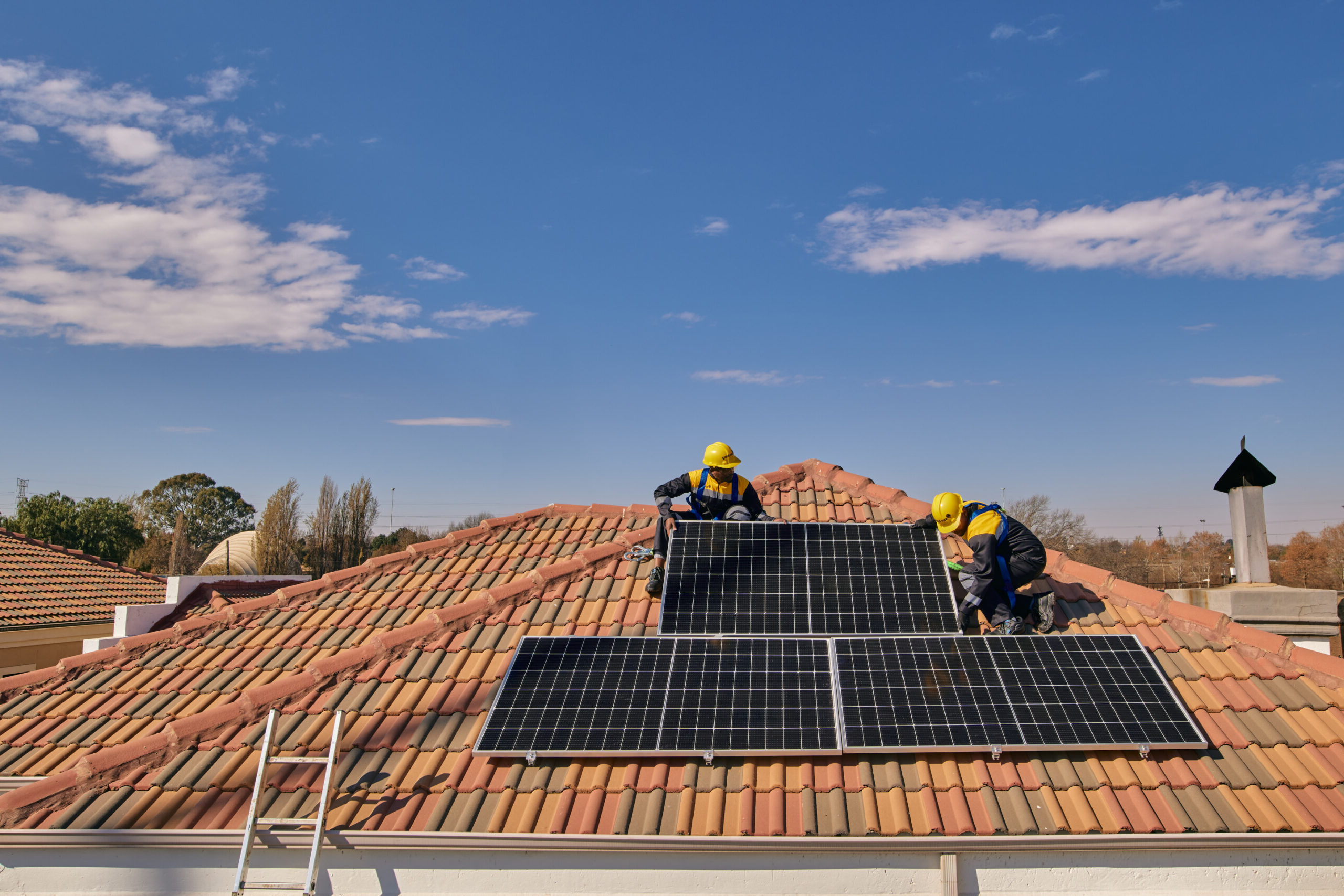 Workers on a tiled roof installing solar panels for a Sun King solar powered rooftop inverter system.