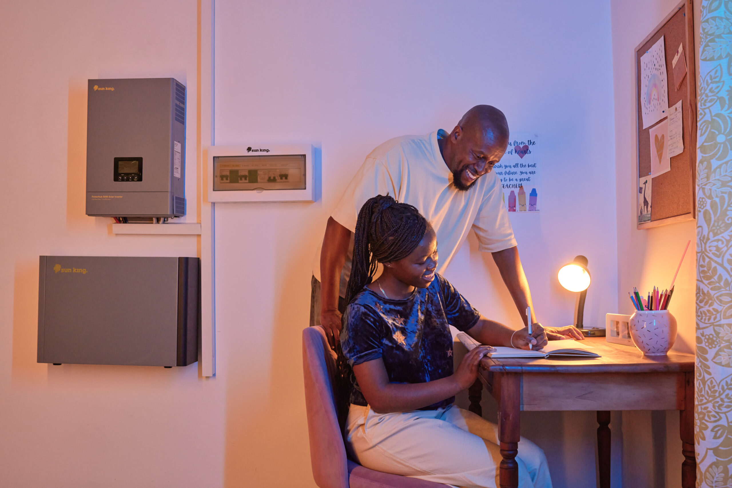 A student does her homework with the help of her father, and the light powered by a Sun King solar powered inverter system.